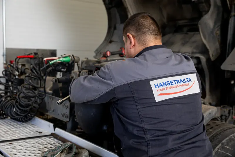 Meistras HTL darbo drabužiais remontuoja puspriekabės ašį ir stabdį